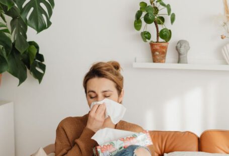 Allergies - Woman Sitting on Sofa and Blowing her Nose into a Tissue