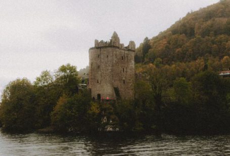 Loch Ness - Scenic view of ancient masonry castle exterior on mountain with trees near Loch Ness lake under misty sky